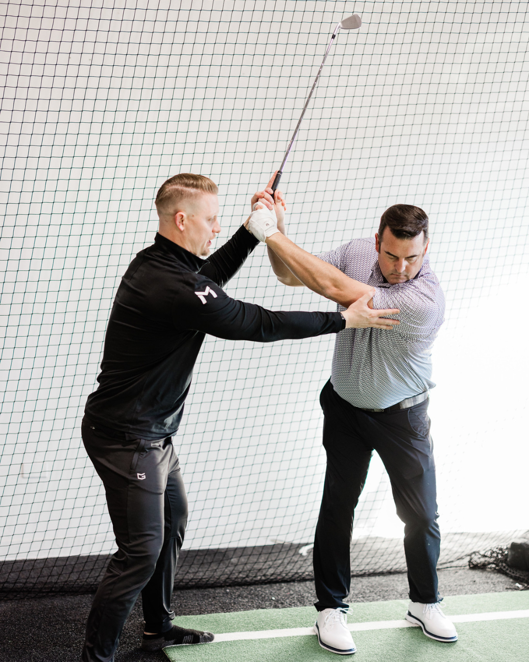 Golf coach assisting a golfer with swing form at Method Athletics